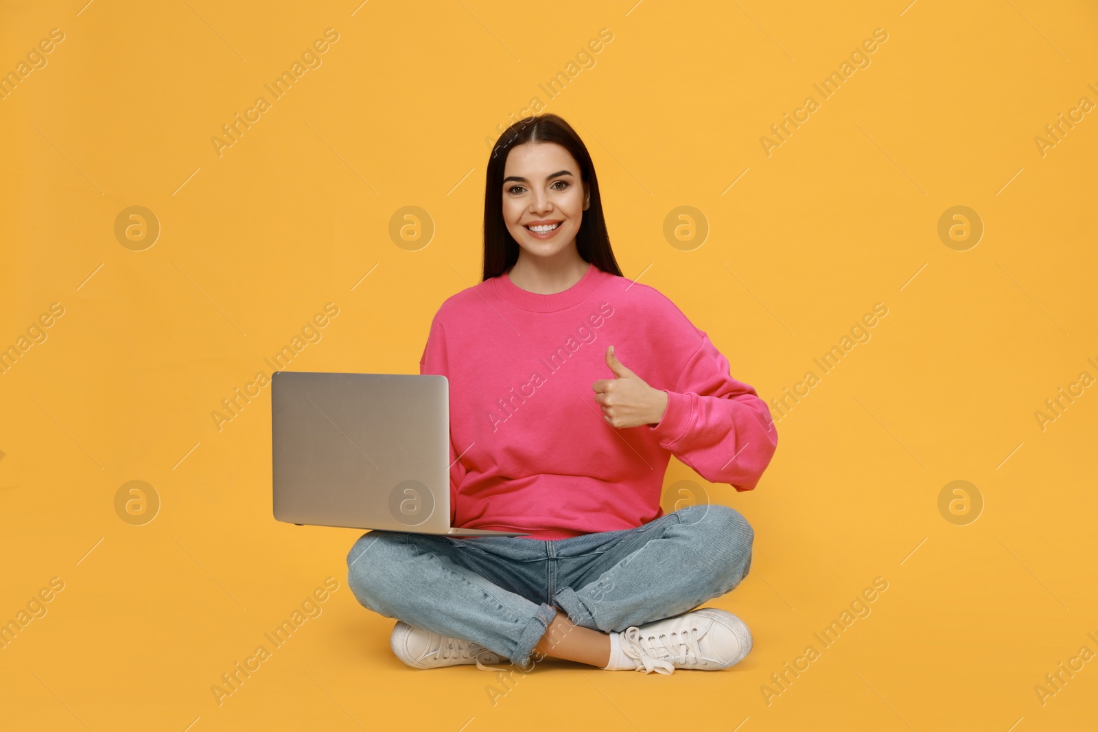 Photo of Young woman with modern laptop on yellow background