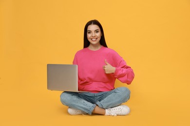 Young woman with modern laptop on yellow background