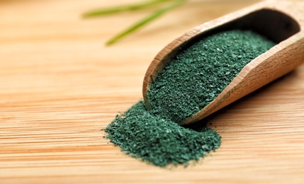 Photo of Scoop of spirulina powder on wooden table, closeup. Space for text