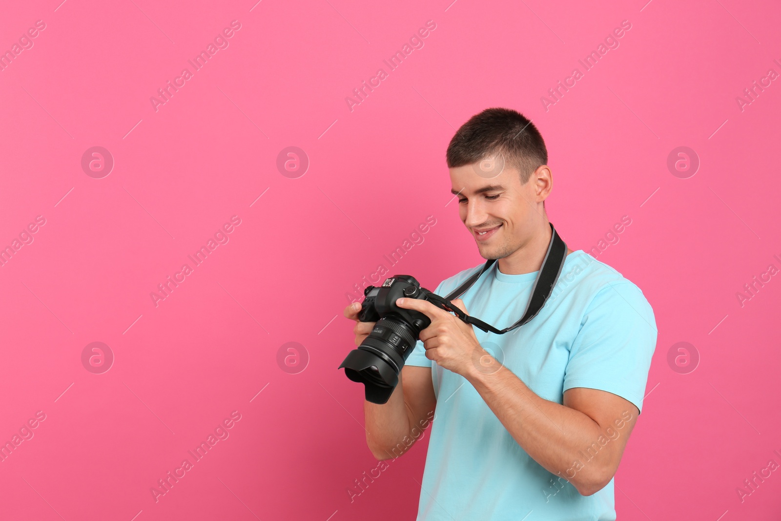 Photo of Young photographer with professional camera on pink background. Space for text