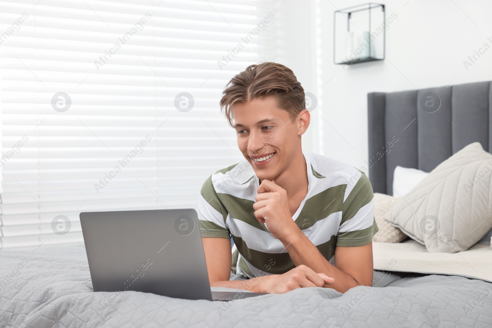 Photo of Happy young man having video chat via laptop on bed indoors