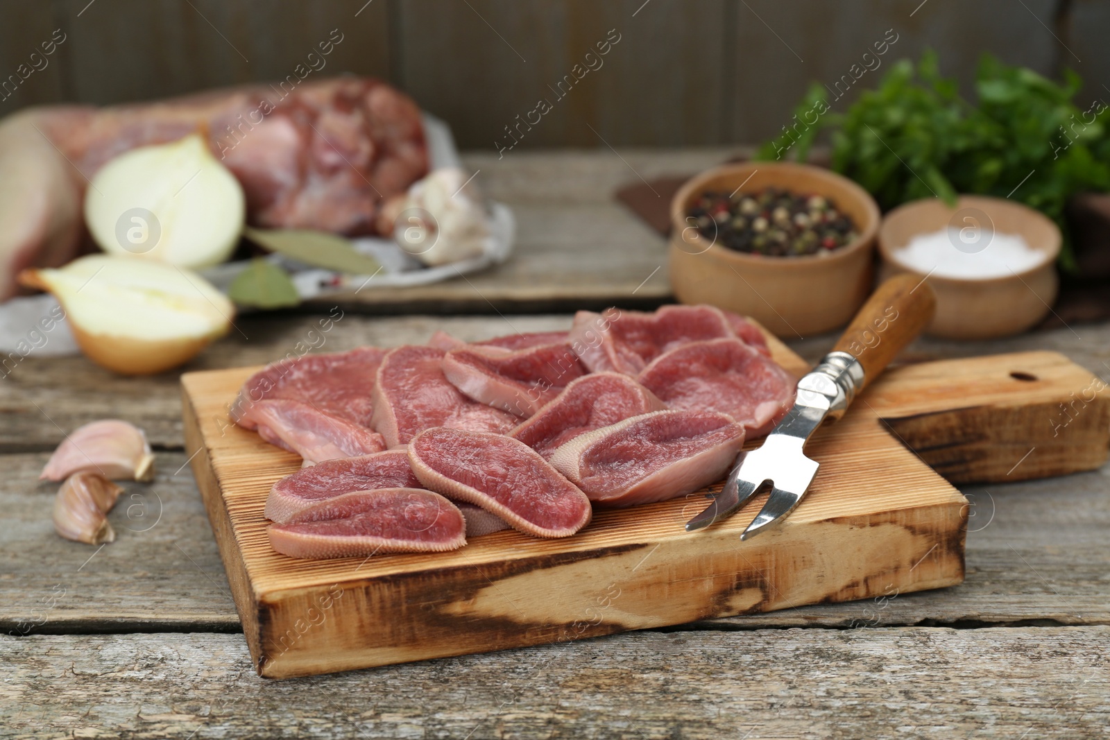 Photo of Board with slices of raw beef tongue and products on wooden table, closeup