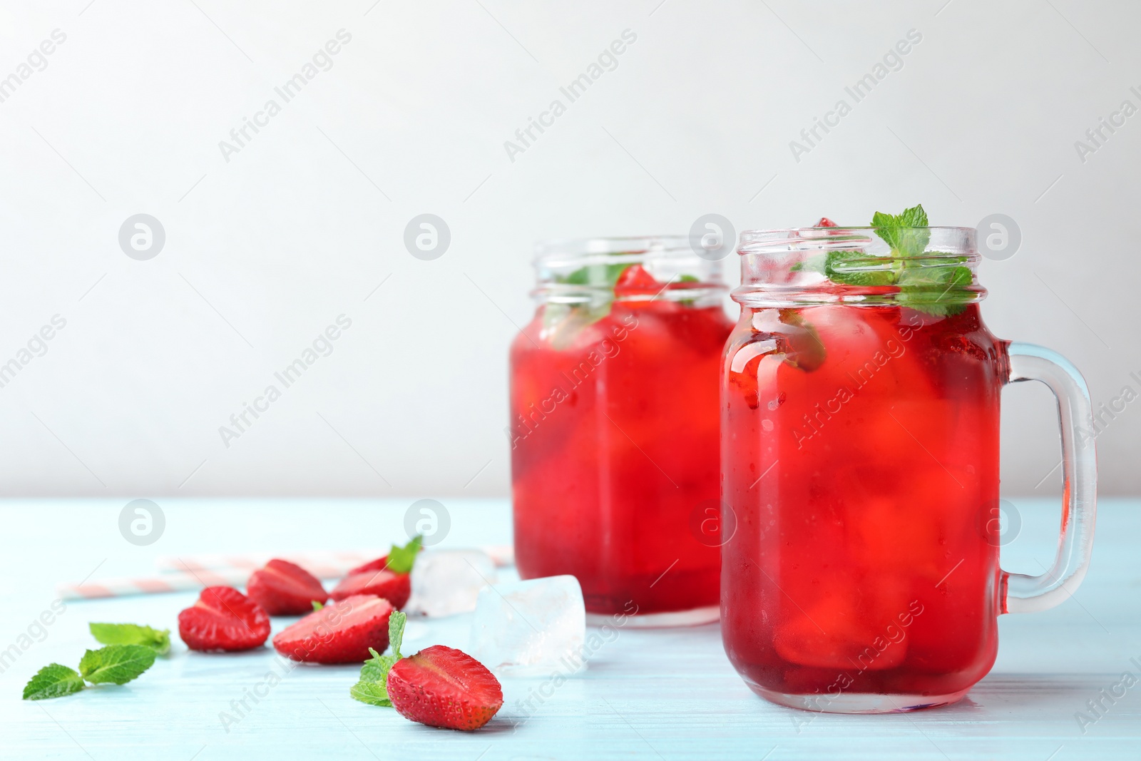 Photo of Mason jars with strawberry refreshing drink on light blue wooden table, space for text