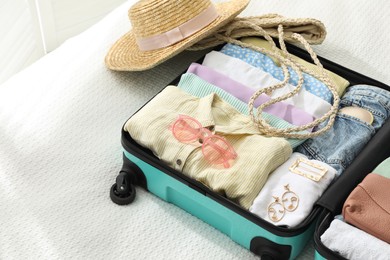 Photo of Open suitcase packed for trip and accessories on bed