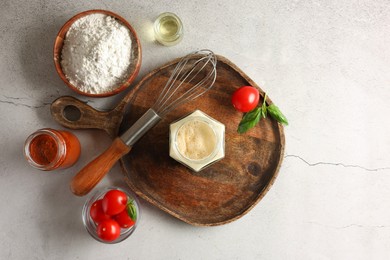 Photo of Pizza dough starter in glass jar, products and whisk on gray textured table, flat lay