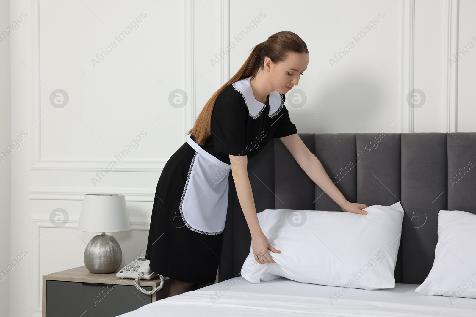 Photo of Young maid making bed in hotel room