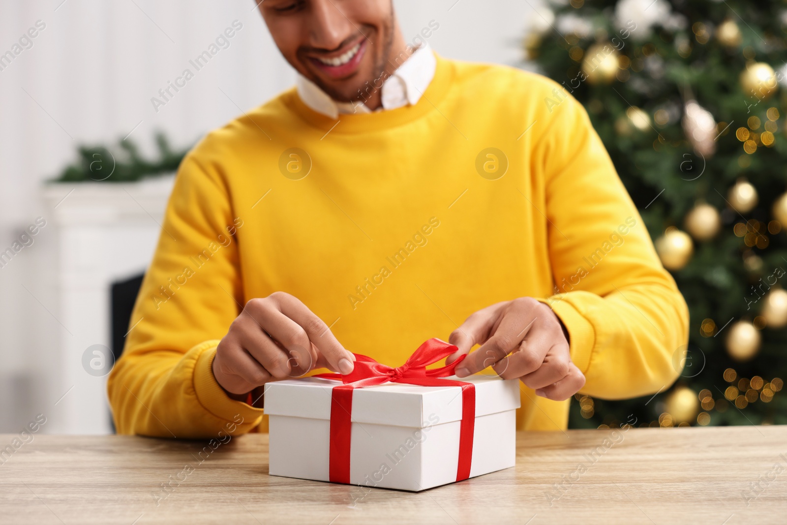 Photo of Man opening Christmas gift at wooden table in room, closeup