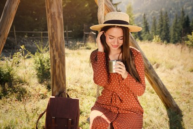 Photo of Young woman with hot drink resting outdoors on sunny day