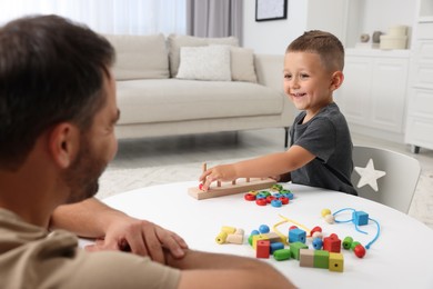 Motor skills development. Father and his son playing with stacking and counting game at table indoors