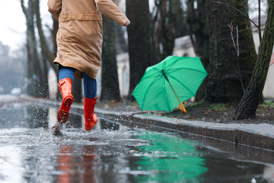 Photo of Woman in rubber boots running after umbrella outdoors on rainy day, closeup