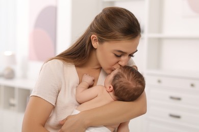 Mother kissing her cute newborn baby indoors