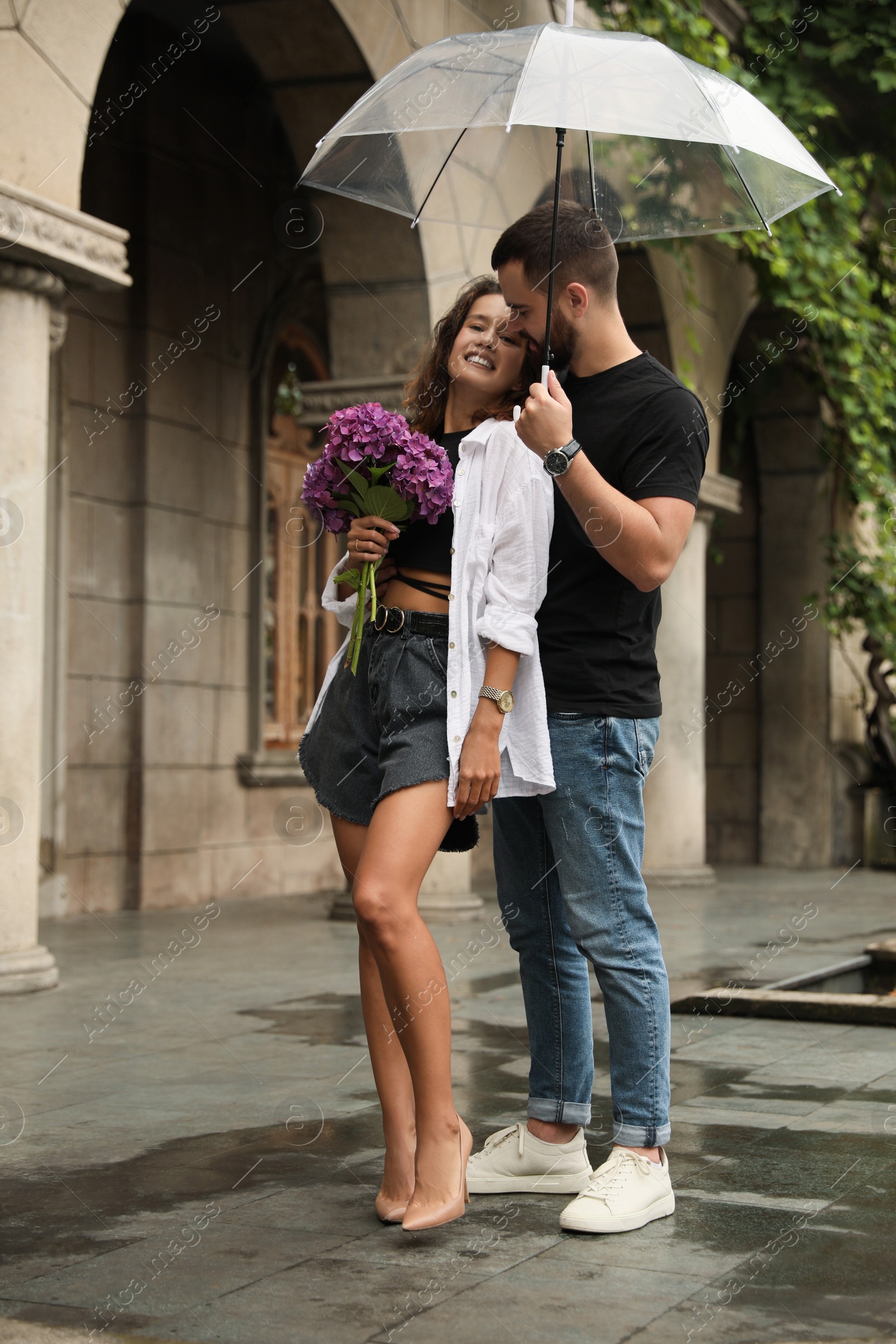 Photo of Young couple with umbrella enjoying time together under rain on city street