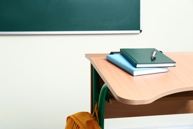 Wooden school desk with stationery near chalkboard in classroom