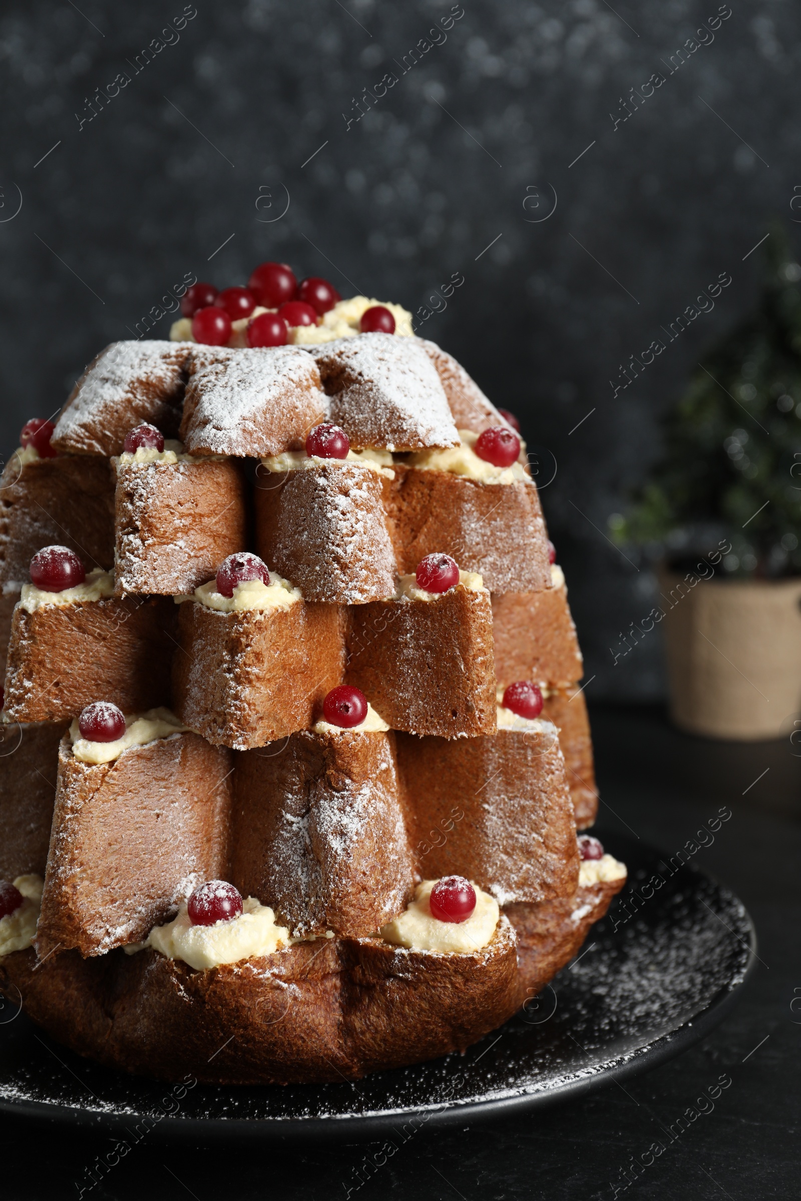 Photo of Delicious Pandoro Christmas tree cake with powdered sugar and berries near festive decor on black table, closeup