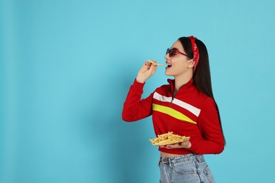 Beautiful young woman eating French fries on light blue background. Space for text