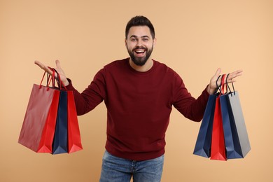 Photo of Happy man with many paper shopping bags on beige background