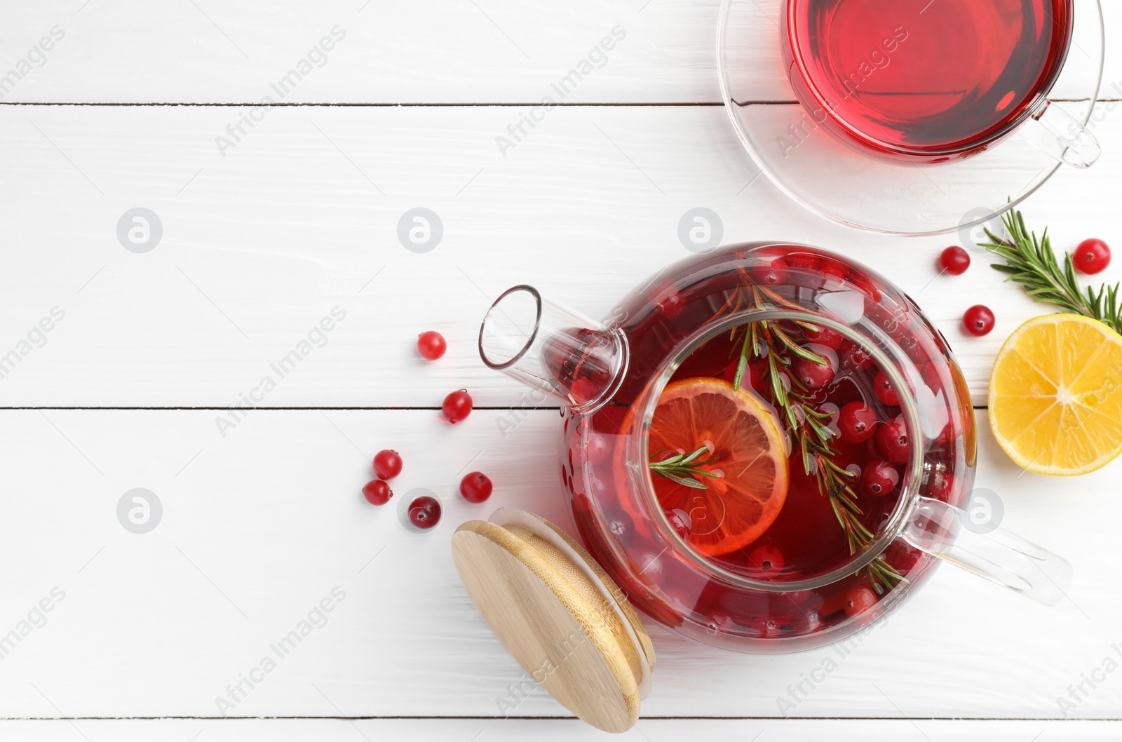 Photo of Tasty hot cranberry tea with lemon, rosemary and fresh berries on white wooden table