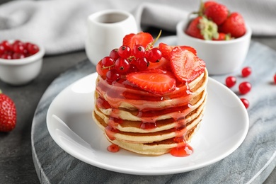 Delicious pancakes with fresh berries and syrup on grey table