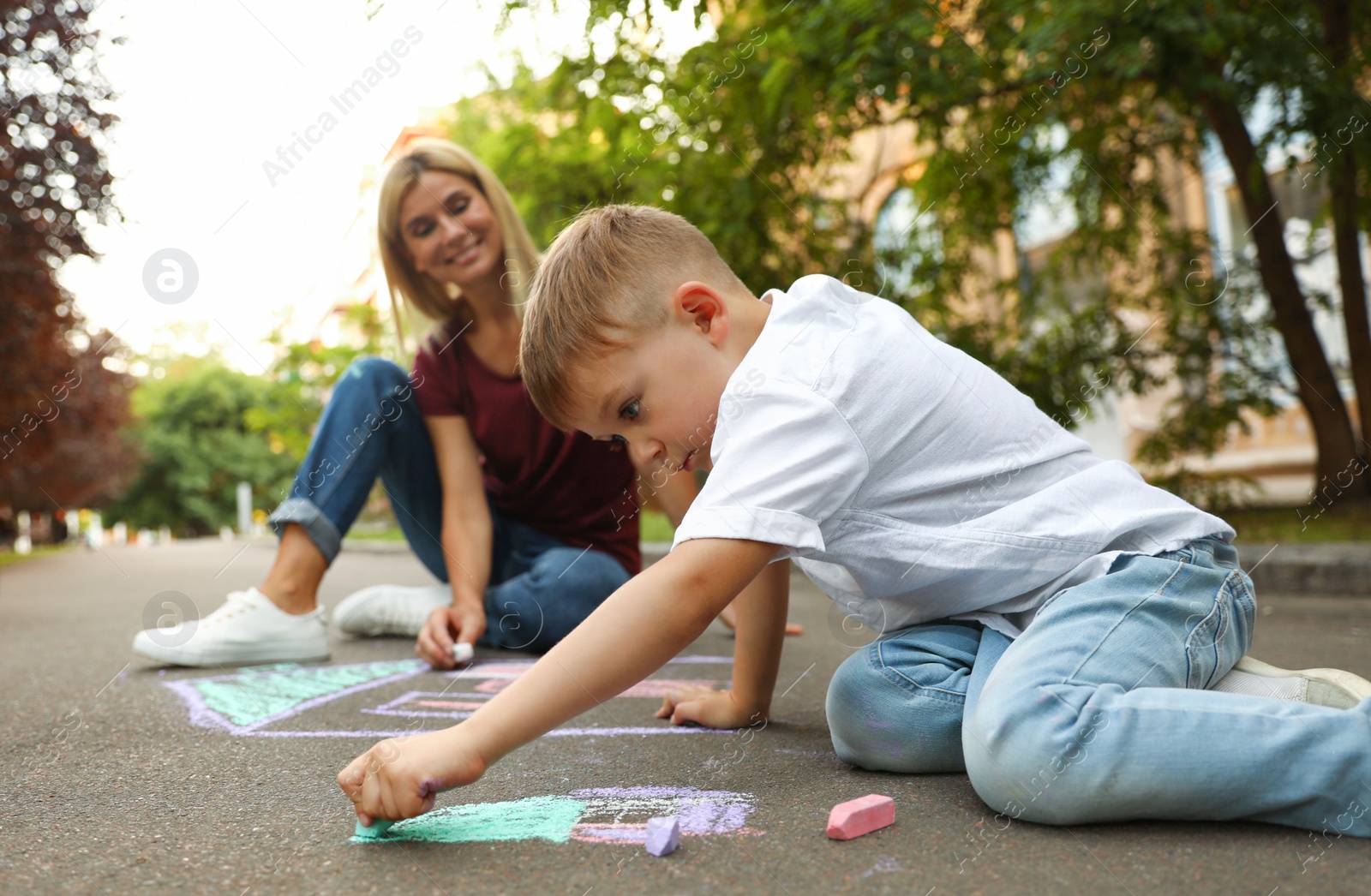 Photo of Nanny with cute little boy drawing house with chalks on asphalt