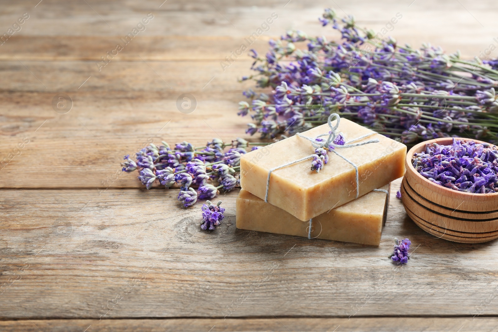 Photo of Handmade soap bars with lavender flowers on brown wooden table. Space for text