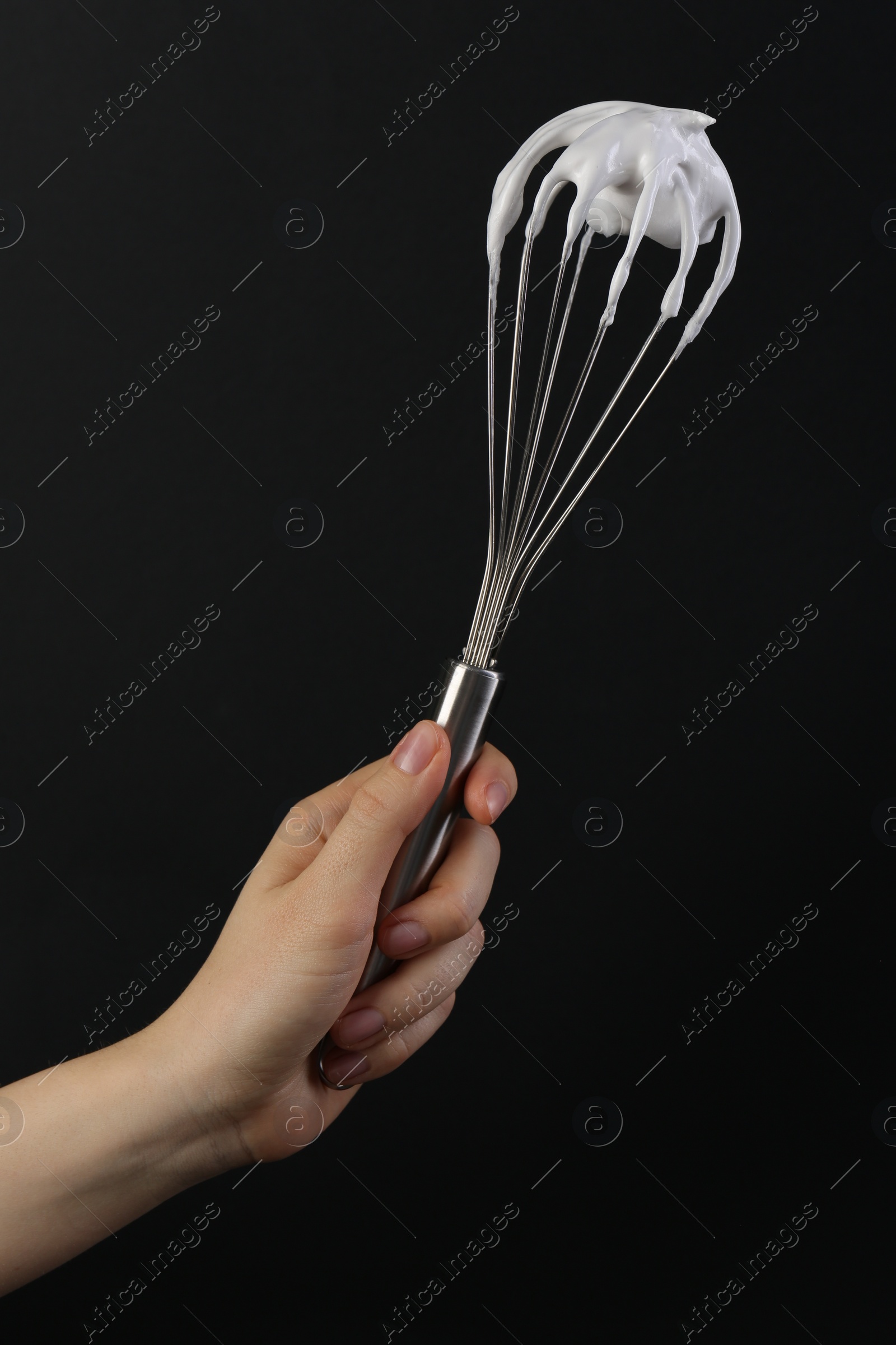 Photo of Woman holding whisk with whipped cream on black background, closeup