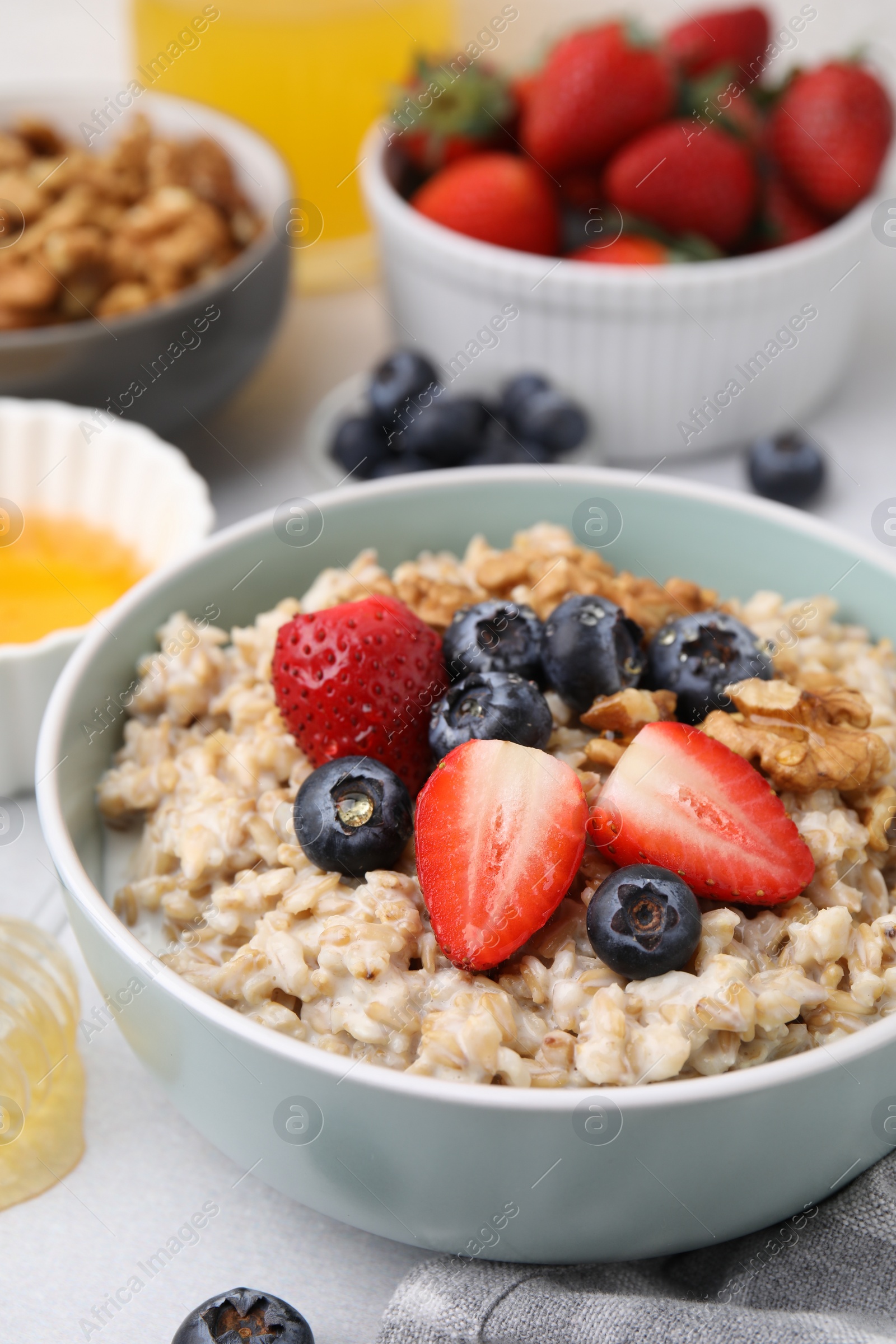 Photo of Tasty oatmeal with strawberries, blueberries and walnuts in bowl on grey table