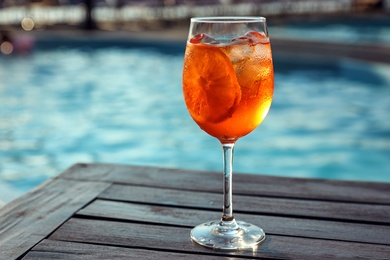 Photo of Glass of fresh summer cocktail on wooden table near swimming pool outdoors