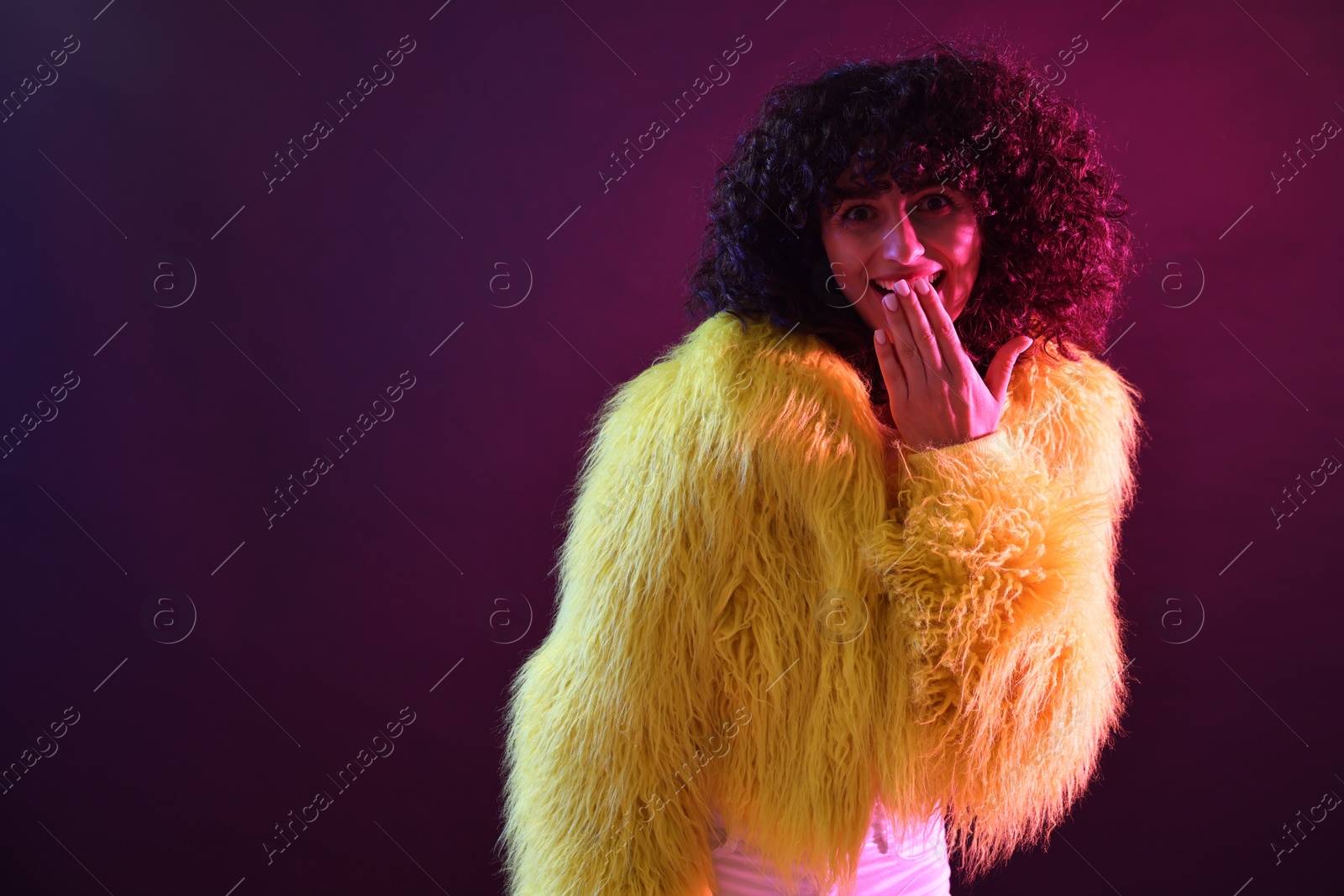 Photo of Beautiful young woman in yellow fur coat on color background in neon lights. Space for text