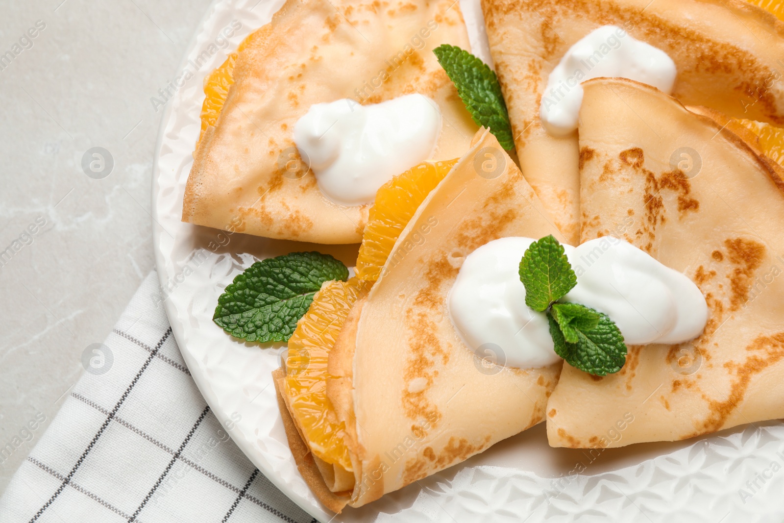 Photo of Delicious thin pancakes with oranges and cream on light table, closeup