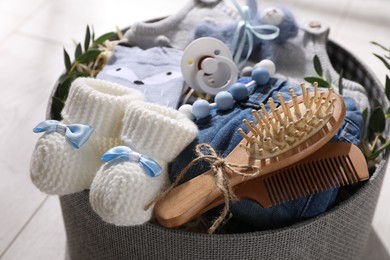 Photo of Box with baby clothes, booties and accessories on wooden floor, closeup