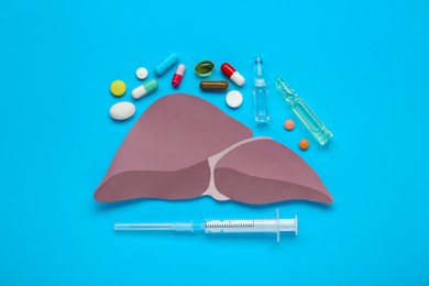 Photo of Paper liver, syringe, vials and pills on light blue background, flat lay. Hepatitis treatment