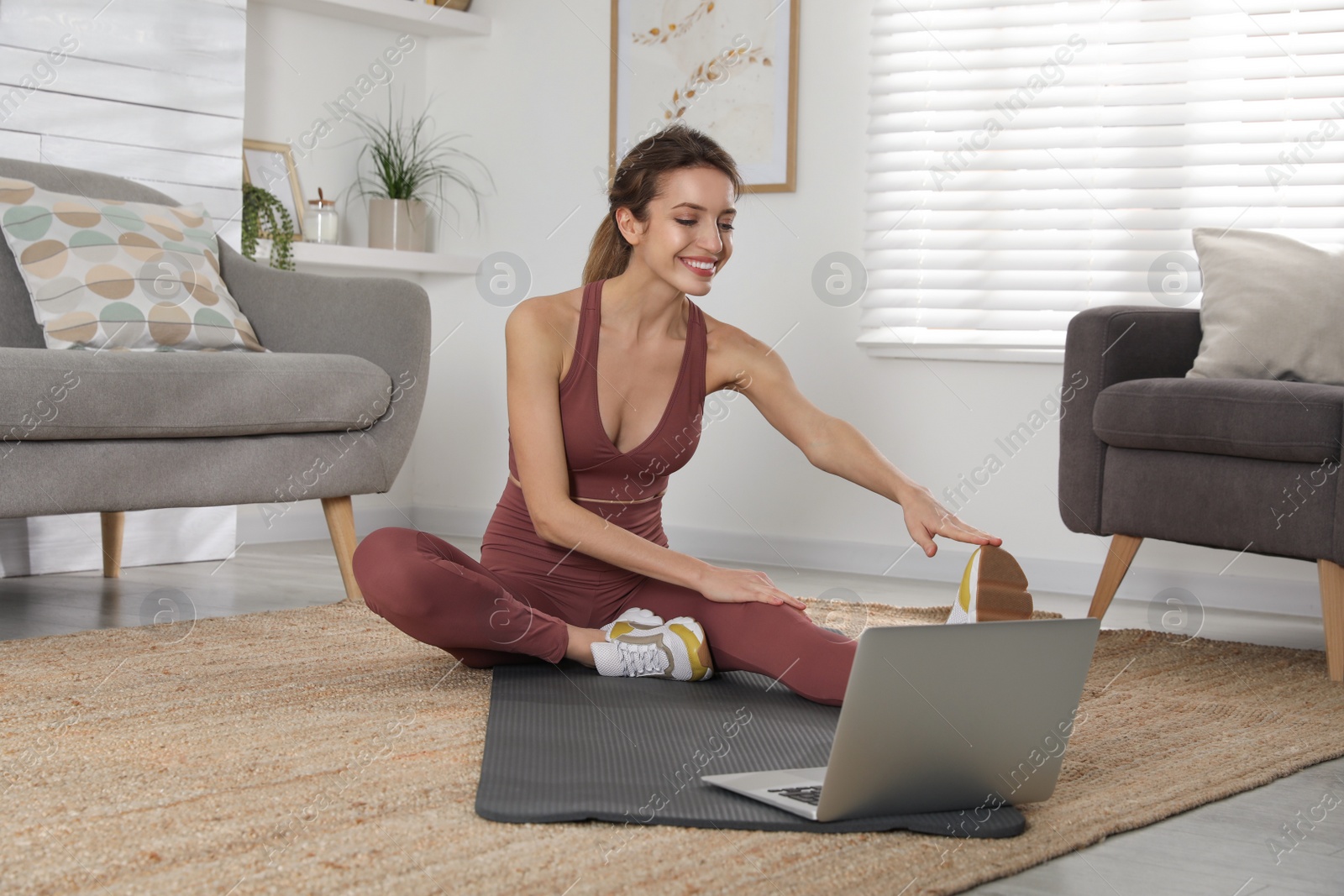 Photo of Beautiful woman stretching on yoga mat while watching online class at home