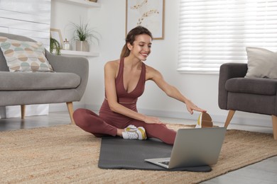 Beautiful woman stretching on yoga mat while watching online class at home