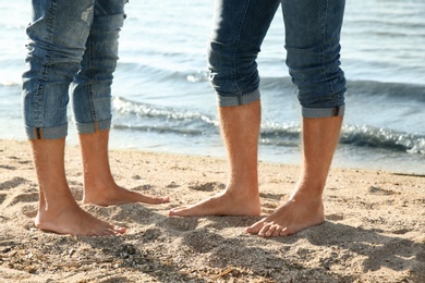 Gay couple standing barefoot on beach, closeup