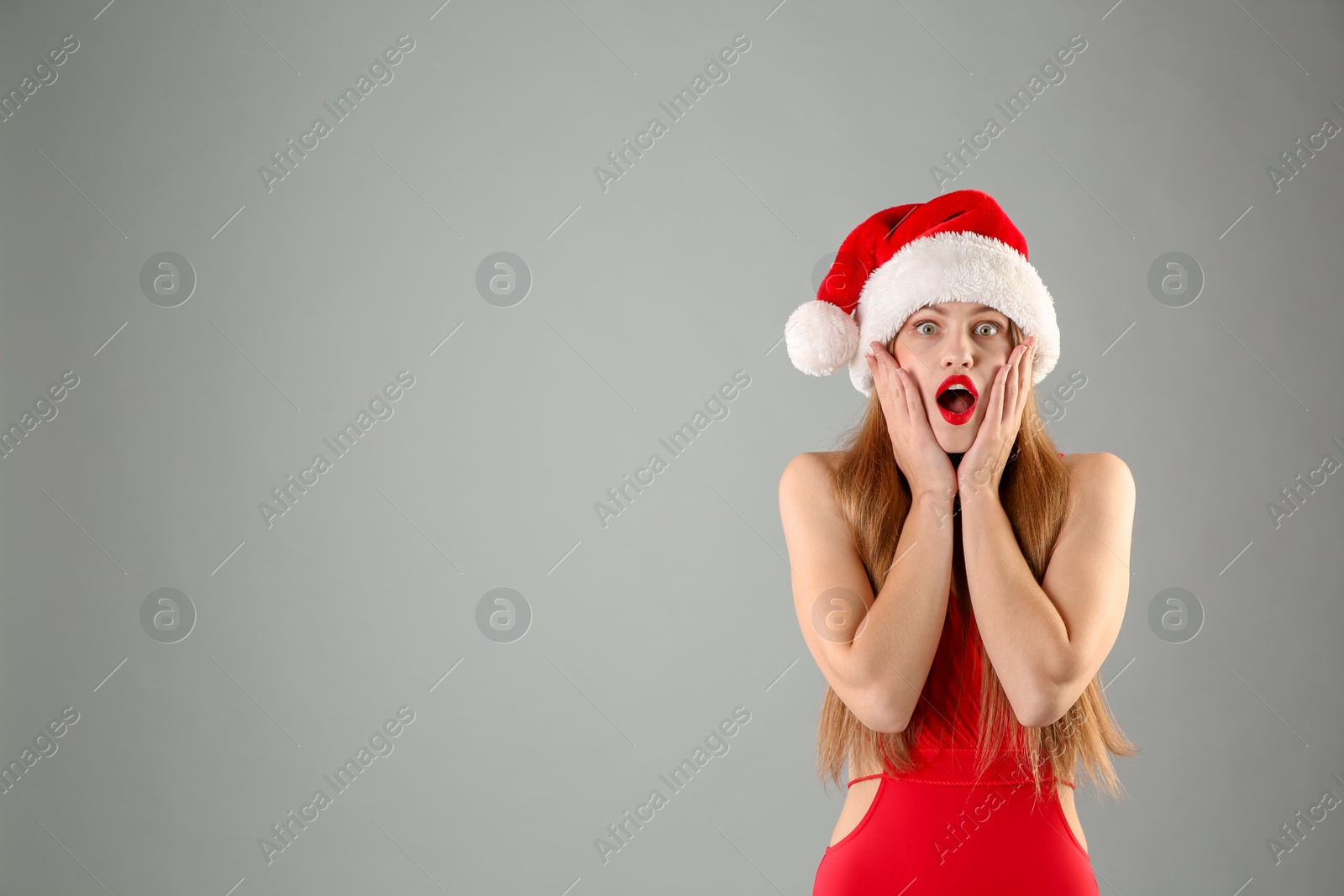 Photo of Young beautiful woman in Santa hat and swimsuit on grey background. Christmas celebration