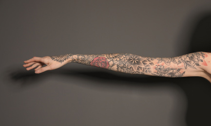 Photo of Woman with colorful tattoos on arm against dark grey background, closeup