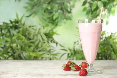 Photo of Tasty fresh milk shake with strawberries on white wooden table against blurred background, space for text