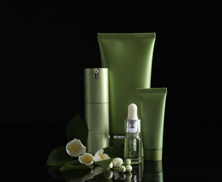 Photo of Set of cosmetic products and flowers on black background
