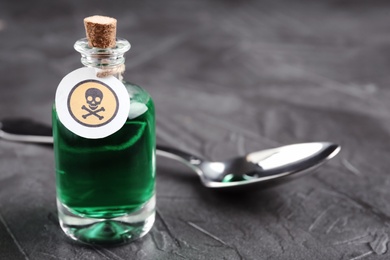 Photo of Glass bottle of poison with warning sign and spoon on grey stone table,  closeup. Space for text