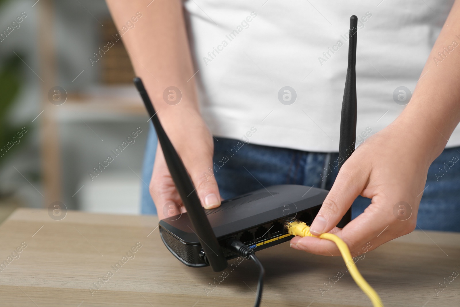 Photo of Woman inserting ethernet cable into Wi-Fi router at table indoors, closeup