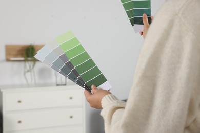 Photo of Woman with paint chips choosing color for wall in room, closeup. Interior design