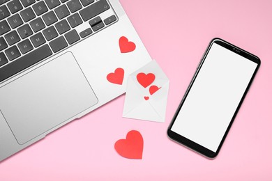 Photo of Long-distance relationship concept. Laptop, smartphone and envelope with paper hearts on pink background, flat lay