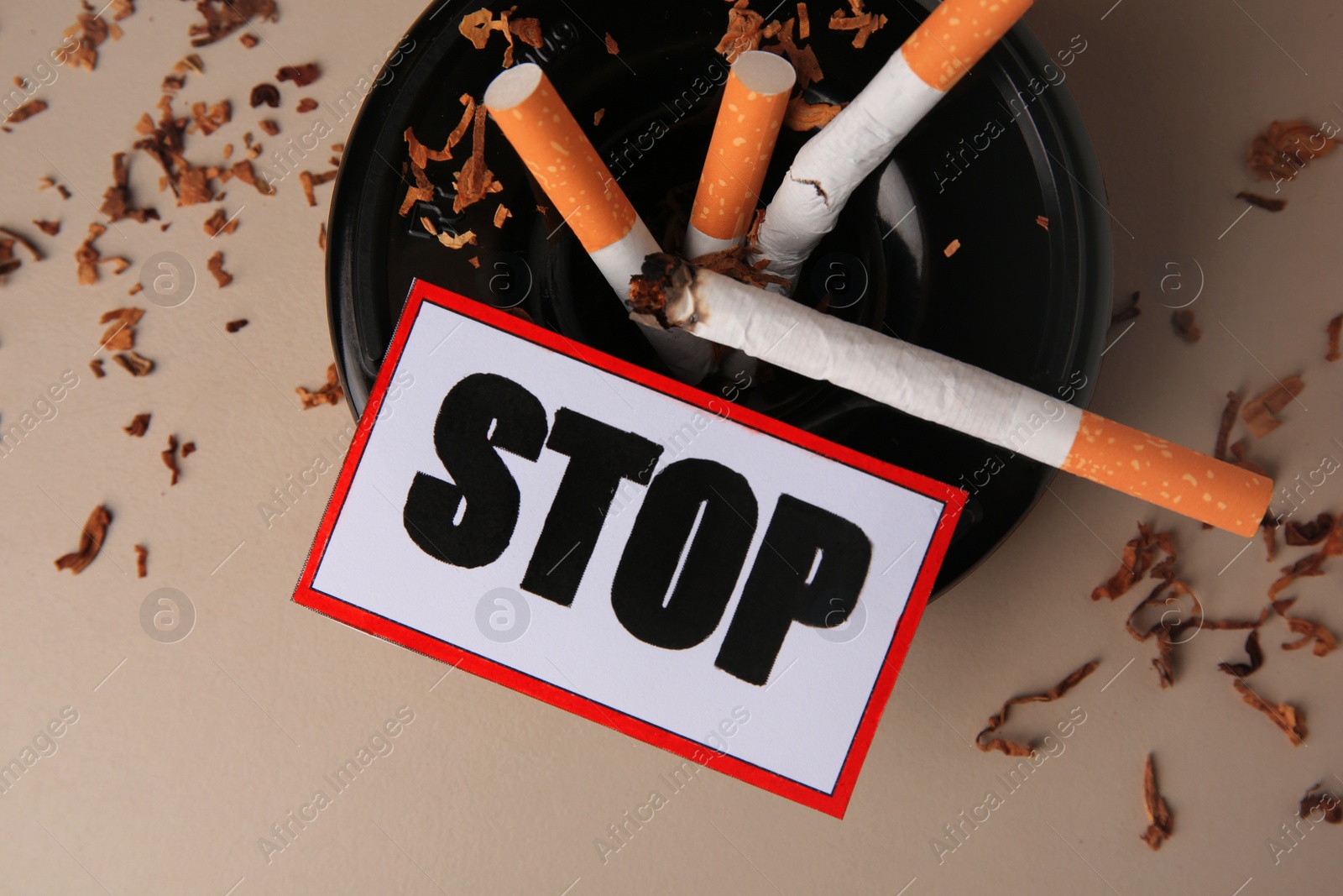 Photo of Card with word Stop, ashtray and cigarette stubs on beige background, flat lay. Quitting smoking concept