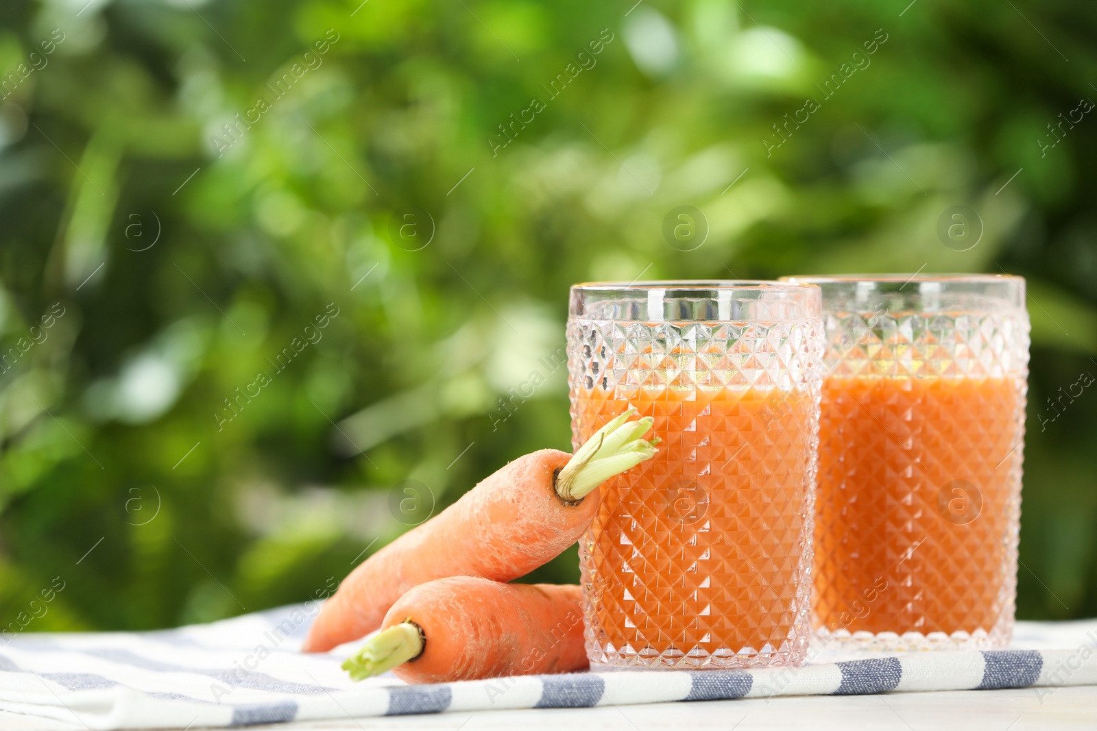 Photo of Glasses of juice and carrots on table against blurred background, space for text