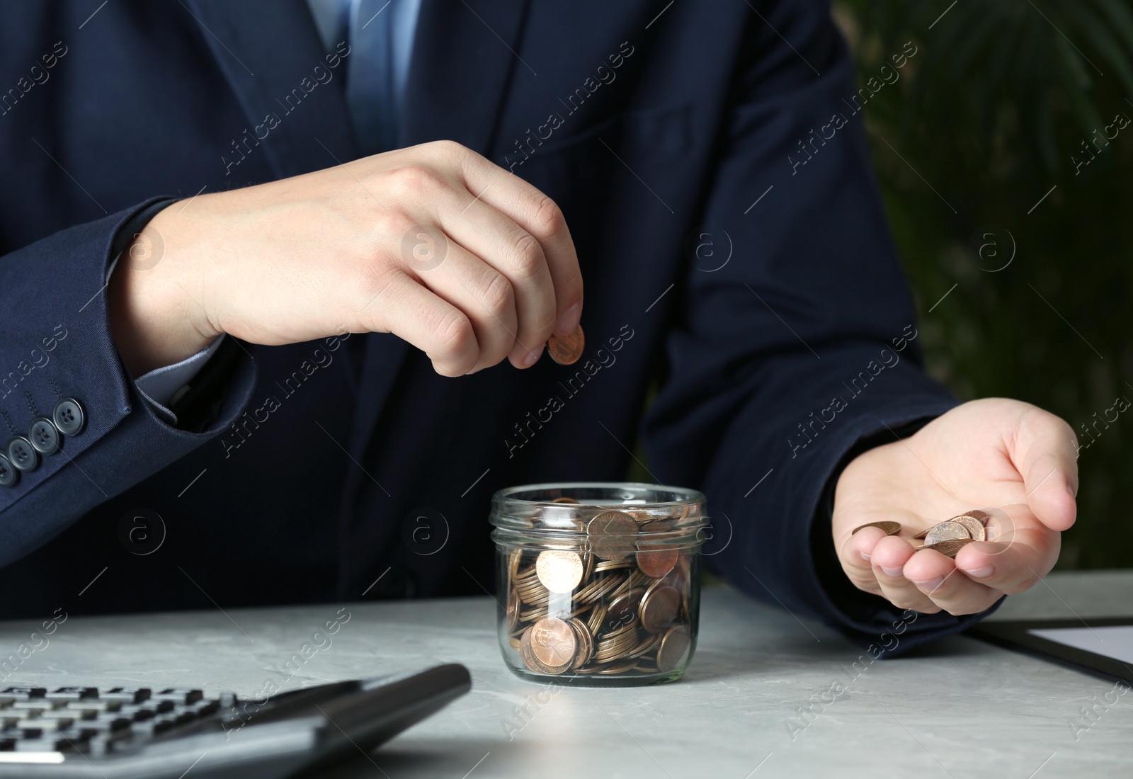 Photo of Man putting coin into jar at grey marble table, closeup. Money savings