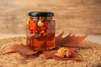 Photo of Different nuts with honey in jar and dry leaf on wicker mat. Space for text