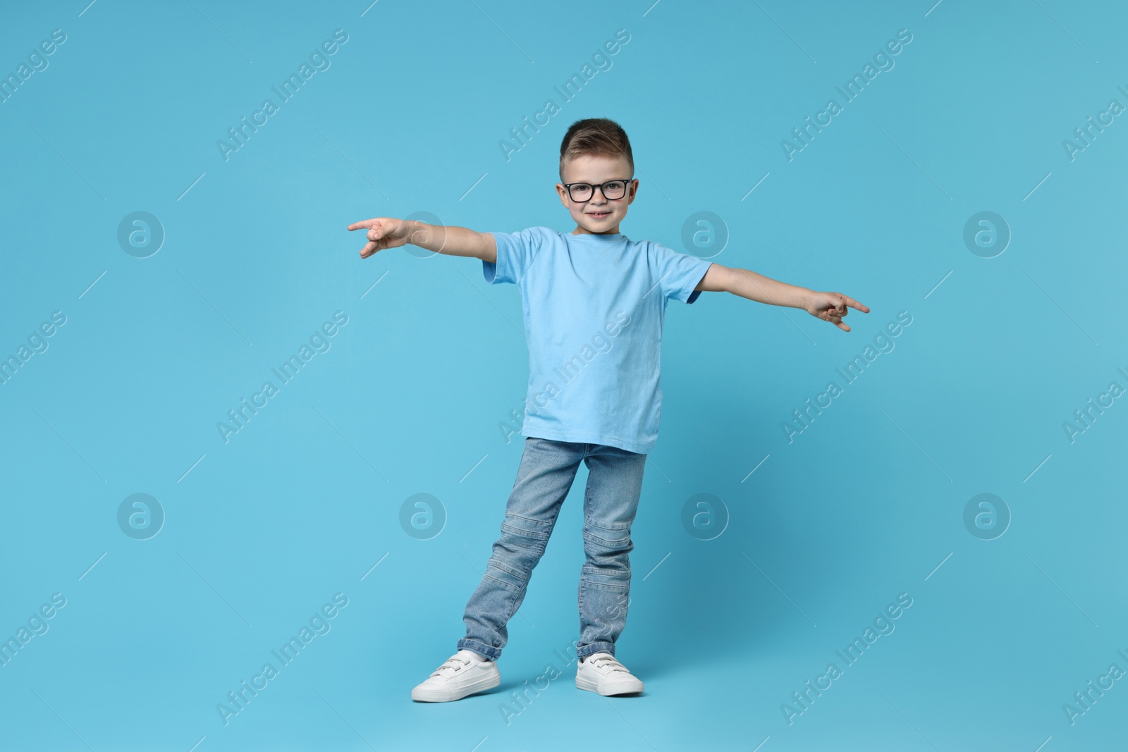 Photo of Happy little boy dancing on light blue background