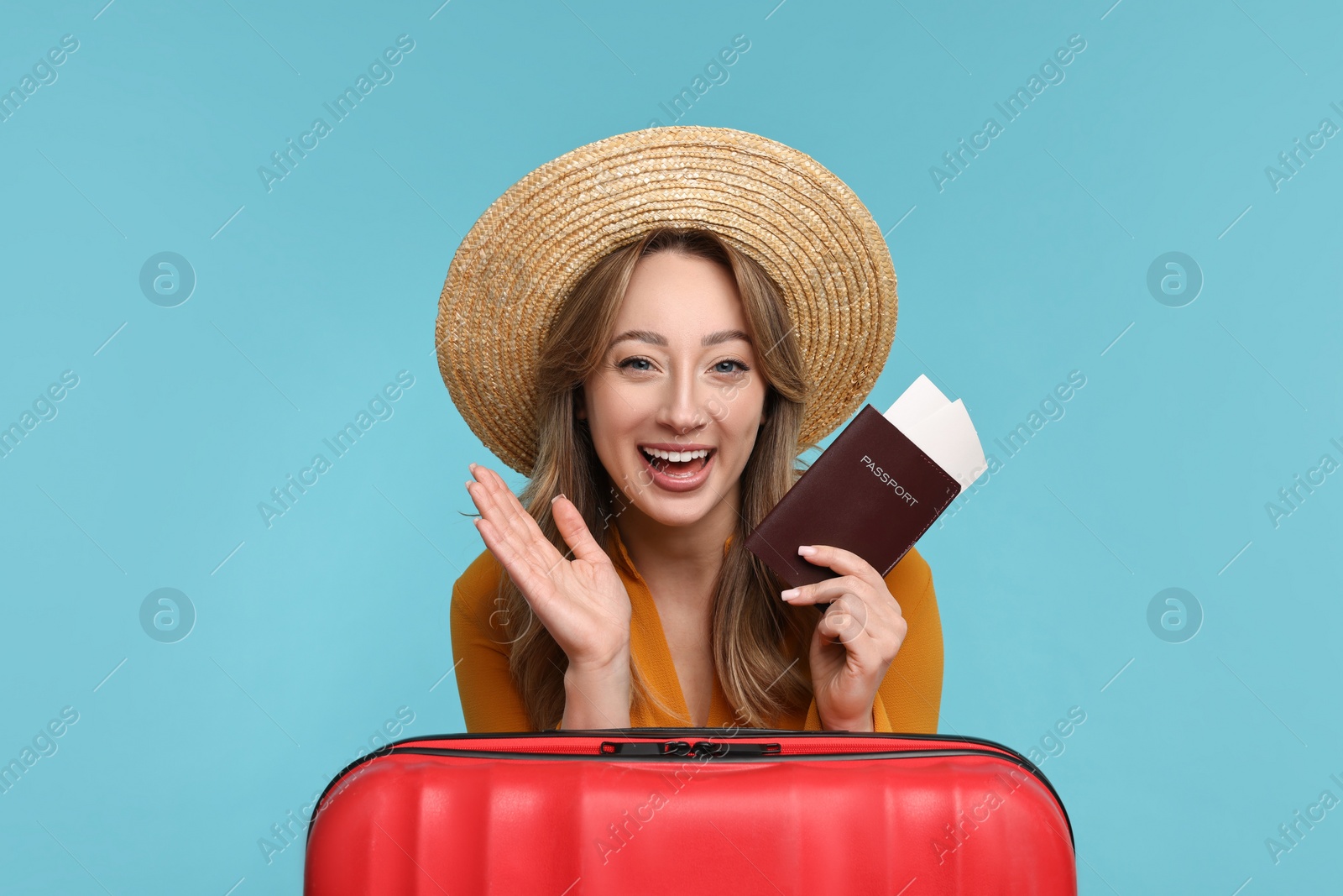 Photo of Happy young woman with passport, ticket and suitcase on light blue background