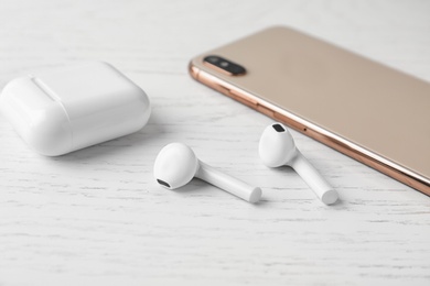 Photo of Wireless earphones, mobile phone and charging case on white wooden table