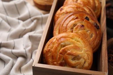 Photo of Delicious rolls with raisins in wooden box on table, closeup and space for text. Sweet buns